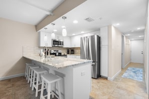A modern kitchen with white cabinetry, stainless steel appliances, and bar stools.