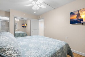 Un dormitorio con una cama, un ventilador de techo, un cuadro y una puerta que da a otra habitación.