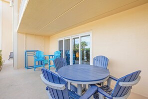 Un patio couvert avec une table ronde et des chaises bleues, une porte-fenêtre coulissante et une vue sur des palmiers.