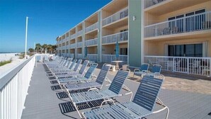Ein Hotel mit mehreren Balkonen, einer langen Reihe von Liegestühlen und Blick auf den Strand.