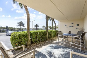Relax in a shaded outdoor seating area with a table and chairs, surrounded by a palm tree and a hedge.