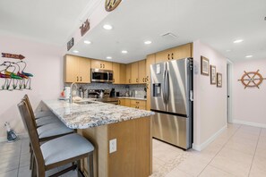 A kitchen with wooden cabinets, a stainless steel refrigerator, a microwave, and a marble countertop.