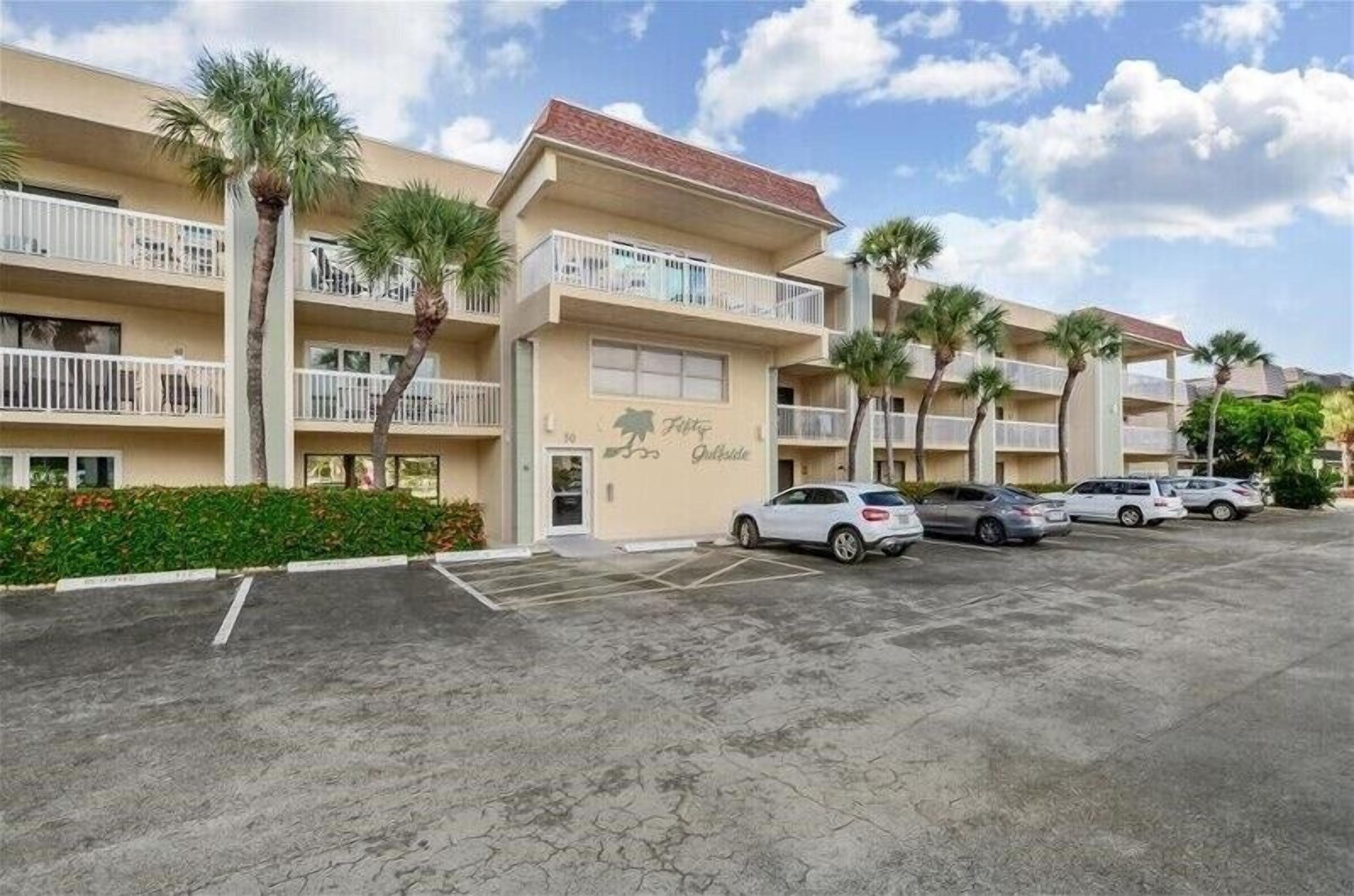 Een meerhoog hotel met balkons, palmbomen en een parkeerplaats.