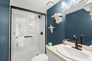 A bathroom with a glass-enclosed shower, a white sink, and a blue accent wall. - 🌴 Coastal Charm Meets Panoramic Beachfront Views – 2BR Corner Unit in Indian Rocks Beach (Indian Rocks Beach)