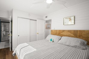 A bedroom with a bed, a wooden headboard, a framed picture on the wall, and a door leading to a bathroom. - 🌴 Coastal Charm Meets Panoramic Beachfront Views – 2BR Corner Unit in Indian Rocks Beach (Indian Rocks Beach)