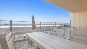 Ein Balkon mit Blick auf den Strand, weiße Möbel und ein Geländer.