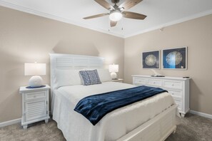 A bedroom with a bed, nightstands, a dresser, a ceiling fan, and wall art.