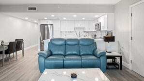 A modern living room with a blue leather sofa, a marble coffee table, and a dining area with chairs and a table.