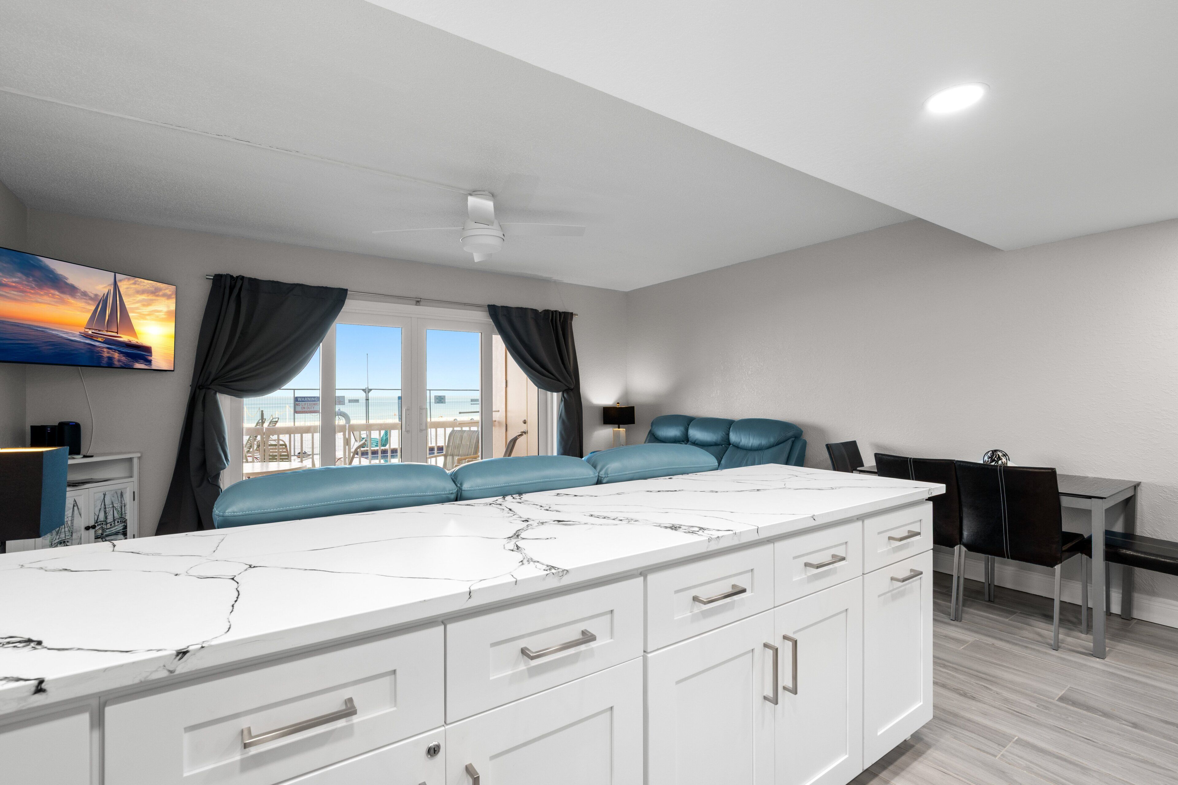 A modern kitchen with a marble countertop, white cabinets, and a view of the sea.