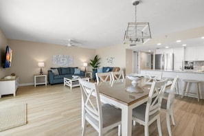 A modern living room with a dining area, a kitchen, and a ceiling fan.