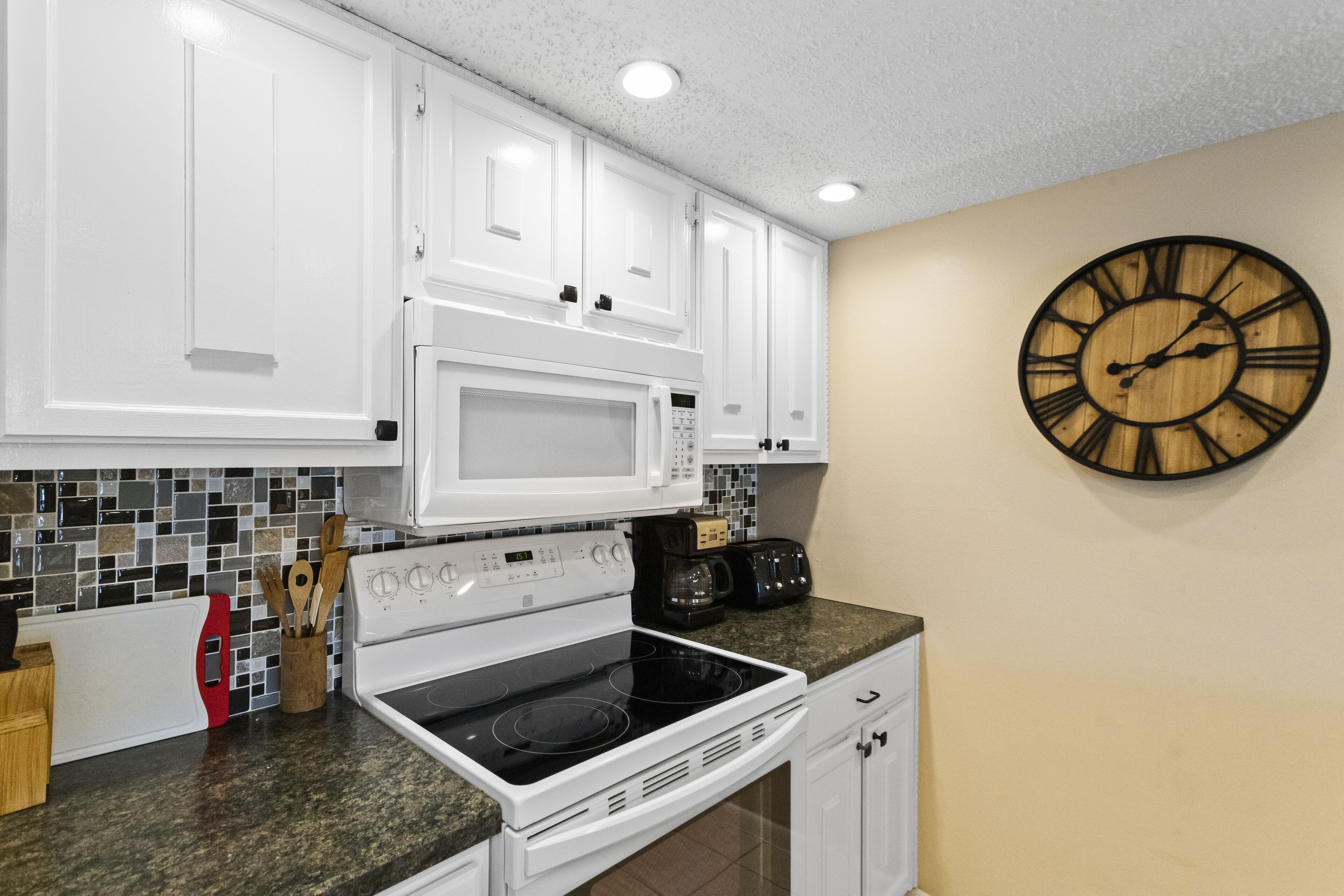 A kitchen with white cabinets, a microwave, a stove, and a wooden clock on the wall.