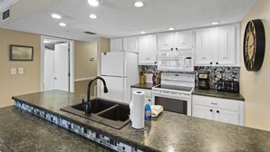 Una cocina moderna con armarios blancos, encimera de granito, un lavabo, microondas y estufa.