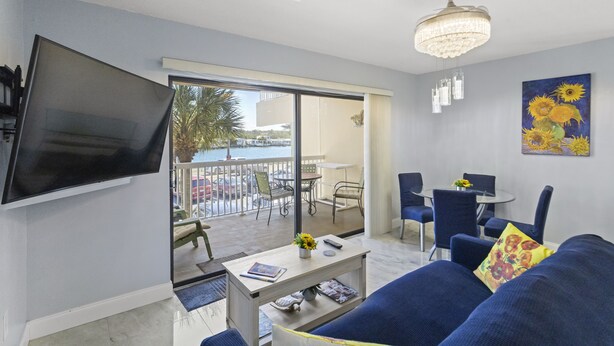 A living room with a TV, sofa, and a balcony with outdoor furniture. - Remodeled 1BR Intracoastal View Condo – Designer Touches, Balcony, & Serene Waterway Setting (Indian Rocks Beach)
