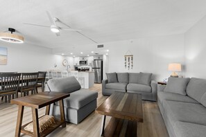 A modern living room with a grey sofa, a wooden coffee table, and a dining area with chairs and a table.