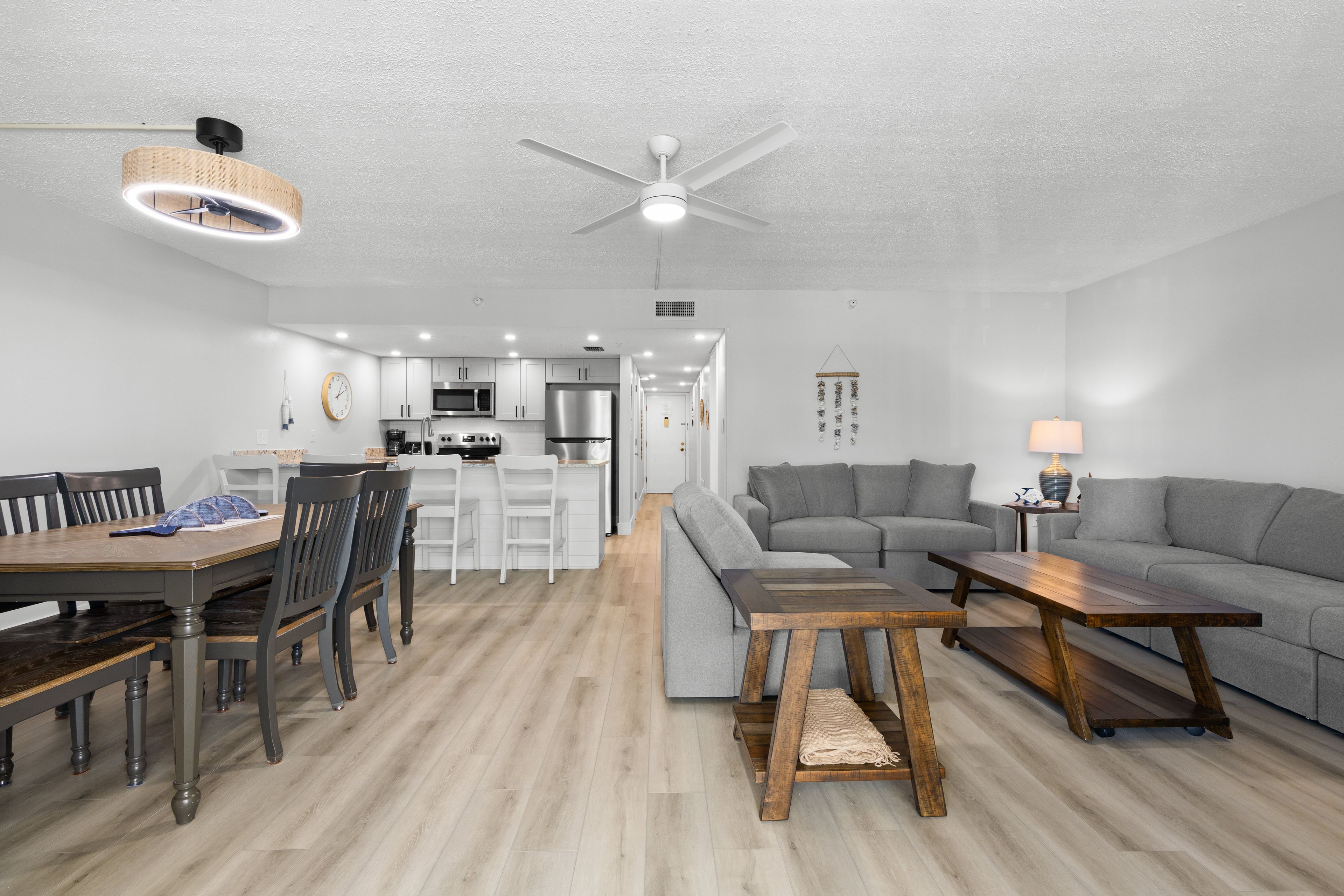 A modern living room with a grey sofa, a wooden coffee table, and a dining area with a wooden table and chairs.