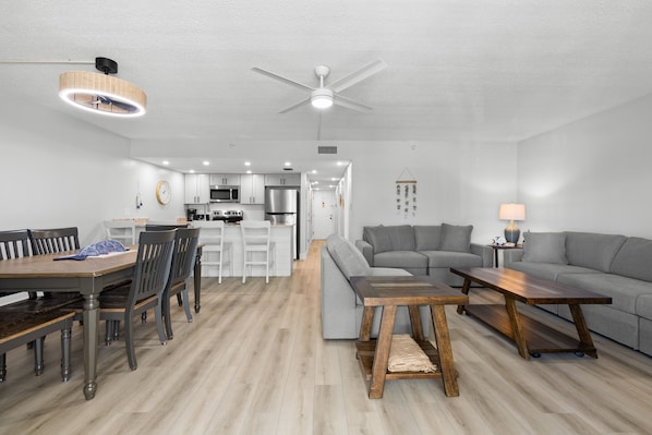 A modern living room with a grey sofa, a wooden coffee table, and a dining area with a wooden table and chairs.