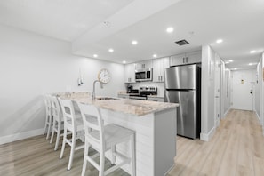 A modern kitchen with white cabinetry, stainless steel appliances, and a marble countertop.
