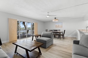 A spacious living area with a wooden table, grey sofa, and a dining set.