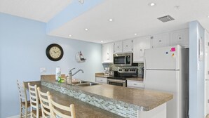 A kitchen with a central island, white cabinets, stainless steel appliances, and a wall clock. - 🌅 Modern 2BR Intracoastal View Condo – Sunrise Balcony & Serene Comfort on Indian Rocks Beach (Indian Rocks Beach)