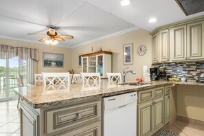 A kitchen with a granite countertop, white cabinets, a dishwasher, and a ceiling fan.