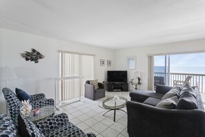 Relax in this stylish living room with a large sofa, armchair, and flat-screen TV, offering a view of the ocean from the balcony.