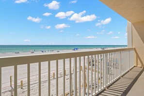 A beach view from a balcony with a white railing, clear sky, and calm sea.