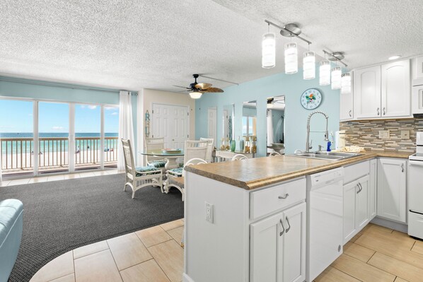 A kitchen with white cabinets, a wooden countertop, and a view of the ocean.