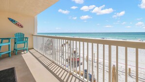 A balcony with a view of the beach, beach chairs, and a surfboard on the wall. - Coastal Charm & Sunset Views from Your Beachfront Balcony at Fifty Gulfside – Indian Rocks Beach (Indian Rocks Beach)