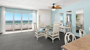 A room with a balcony, a ceiling fan, a dining table with chairs, and a view of the ocean. - Coastal Charm & Sunset Views from Your Beachfront Balcony at Fifty Gulfside – Indian Rocks Beach (Indian Rocks Beach)