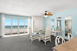 A room with a balcony, a ceiling fan, a dining table with chairs, and a view of the ocean.