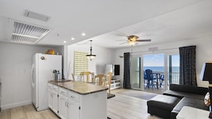 A modern kitchen with white cabinets, a refrigerator, and a dining area with wooden chairs and a table.