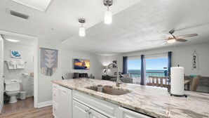 Una cocina moderna con una isla grande, un ventilador de techo y vista al océano.