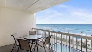 Ein Balkon mit rundem Tisch und vier Stühlen, der Blick auf Strand und Pool geht.