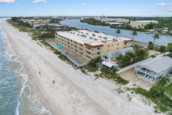 An aerial view of a beachfront hotel with multiple buildings, a swimming pool, and a river nearby.