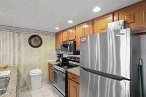 A kitchen with wooden cabinets, a stainless steel refrigerator, a microwave, and a clock on the wall.