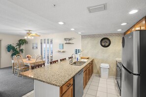 A kitchen with granite countertops, wooden cabinets, a stainless steel refrigerator, a sink, and a ceiling fan.