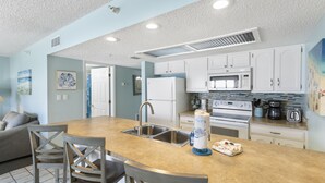 A kitchen with a central island, stainless steel sink, white cabinets, and a microwave. - Corner Retreat with Gulf & Intracoastal Views from Wraparound Balcony at Fifty Gulfside (Indian Rocks Beach)