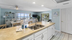 A modern kitchen with a large island, white cabinetry, and a view of the ocean. - Corner Retreat with Gulf & Intracoastal Views from Wraparound Balcony at Fifty Gulfside (Indian Rocks Beach)