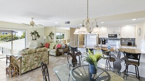 Amplia sala de estar con una mesa de comedor de vidrio, un sofá y una cocina al fondo.