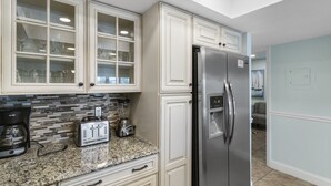 Una cocina con muebles blancos, un refrigerador de acero inoxidable, un tostador y una cafetera.
