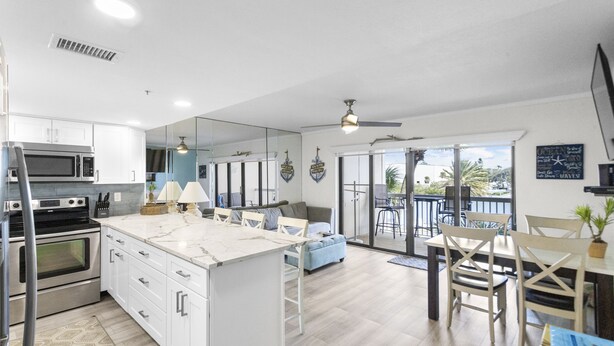 Una cocina moderna con armarios blancos, una isla grande y un comedor con vista a un balcón.