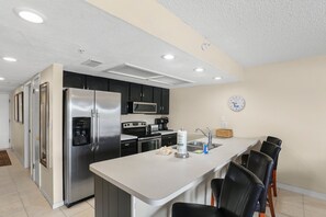 A modern kitchen with a refrigerator, microwave, oven, and a small dining area with chairs.