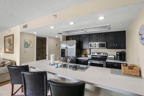 Una cocina moderna con electrodomésticos de acero inoxidable, una isla central con taburetes y un comedor con sofá y sillas.