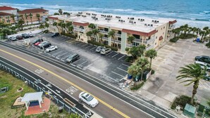 Un hotel frente a la playa con estacionamiento, una calle con carril bici y vista al océano.