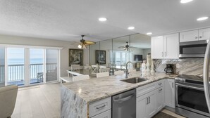 A modern kitchen with a marble countertop, stainless steel appliances, and a view to the outside.