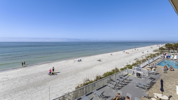 A beach view from a balcony with a pool area and lounge chairs.