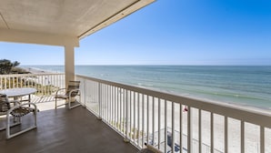 A balcony with a view of the ocean, a table, and two chairs.