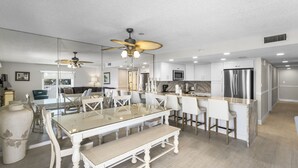 A modern kitchen with white cabinetry, a central island with bar stools, a glass dining table, and a ceiling fan.
