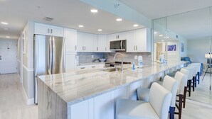 Een moderne keuken met witte kasten, roestvrijstalen apparatuur, een marmeren aanrechtblad en een bar voorzien van witte barstoelen.