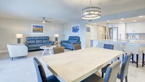 Een moderne woonkamer met een eethoek, met een grote tafel, blauwe banken en een plafondventilator.
